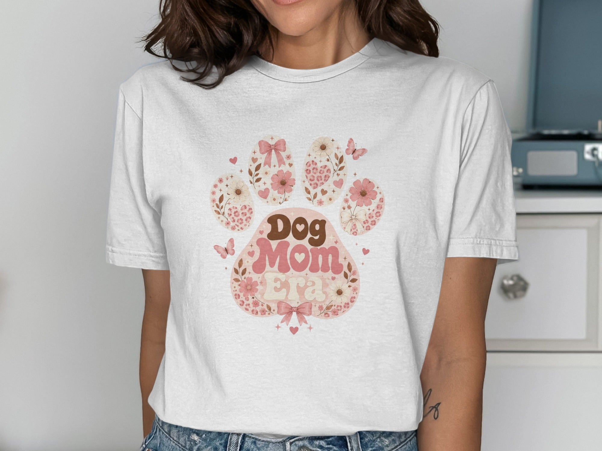 White t-shirt with a pink paw print design saying "Dog Mom Era".