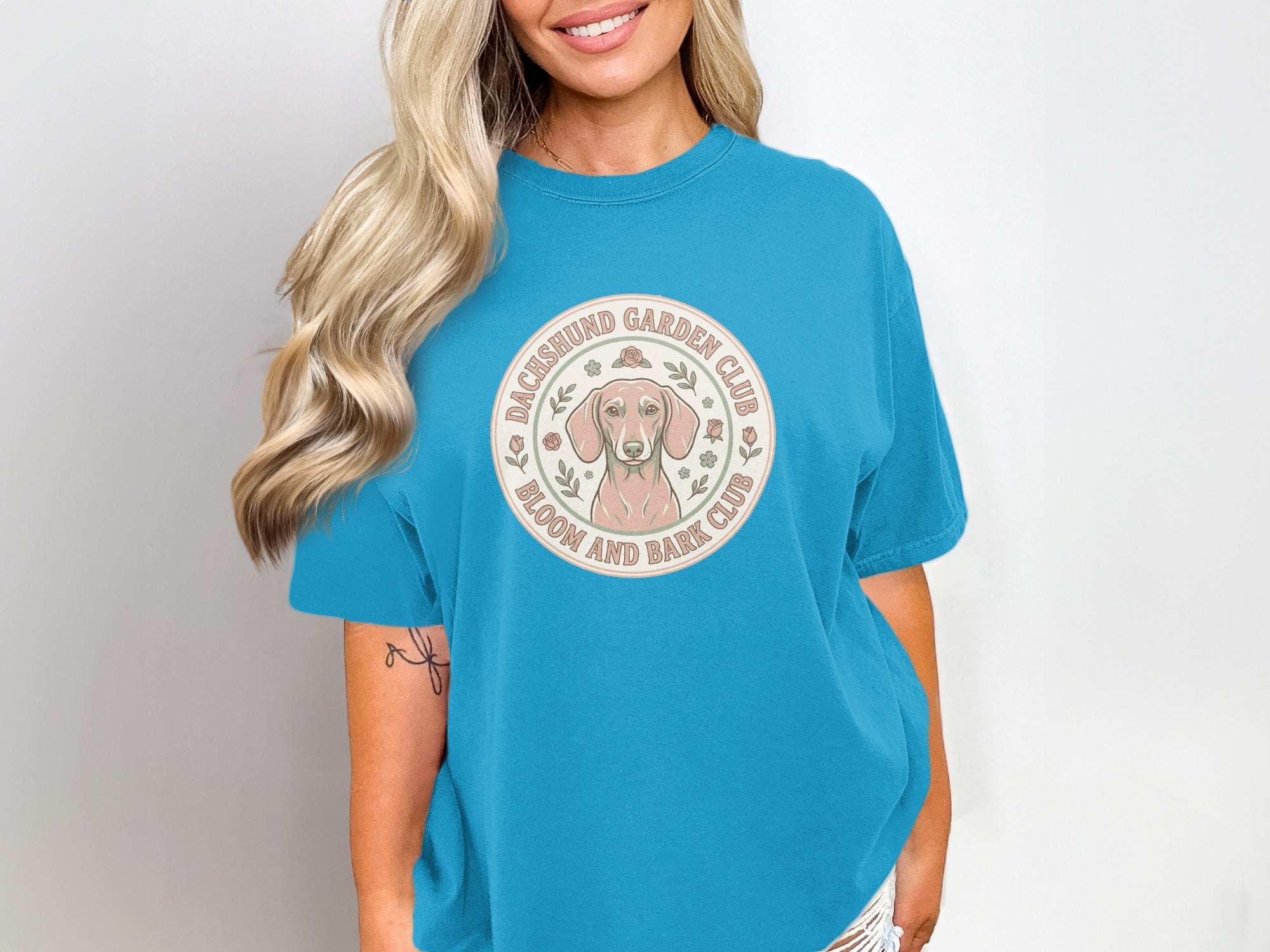Dachshund Garden Club circular logo with dog and floral accents on blue t-shirt.